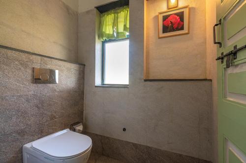 a bathroom with a toilet and a window at SaffronStays Lake House Marigold, Nashik - rustic cottages with private plunge pool in Nashik