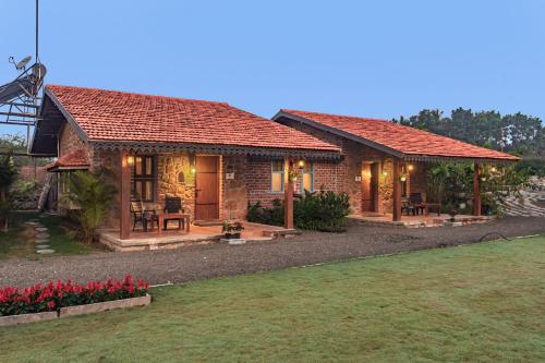 a small house with red flowers in front of it at SaffronStays Lake House Marigold, Nashik - rustic cottages with private plunge pool in Nashik