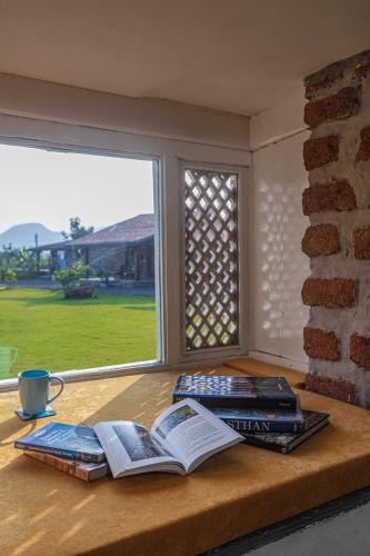 a table with books on it with a window at SaffronStays Lake House Marigold, Nashik - rustic cottages with private plunge pool in Nashik