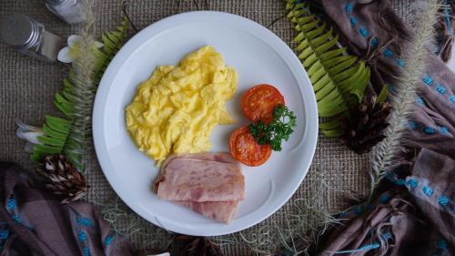 a plate with eggs ham and tomatoes on a table at Louto Dmell Villa & Guesthouse in Sanur