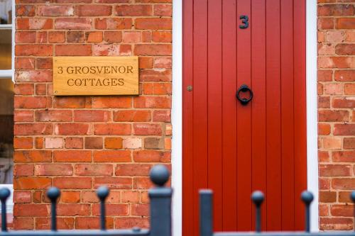 a red door and a sign next to a brick wall at Country Charm Cottage Sleeps 4 & Free Parking in Chester