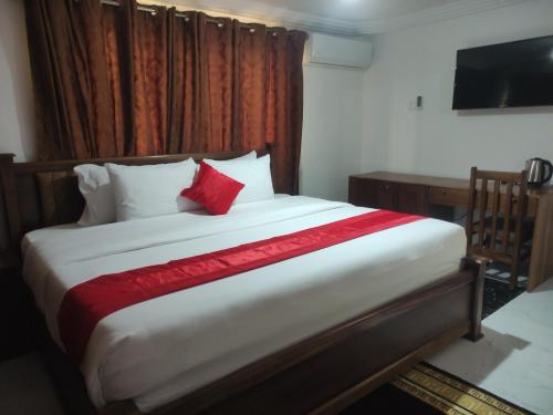 a bedroom with a large bed with red pillows and a desk at Bassi Hotel in Takoradi