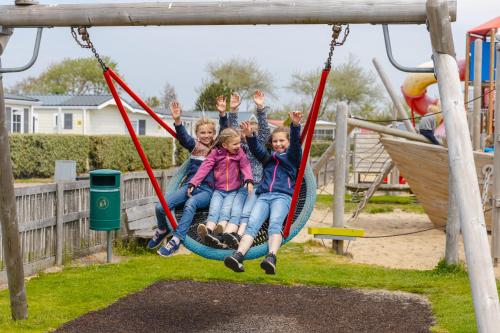 four children sitting on a swing at a playground at Strandcamping Valkenisse in Biggekerke