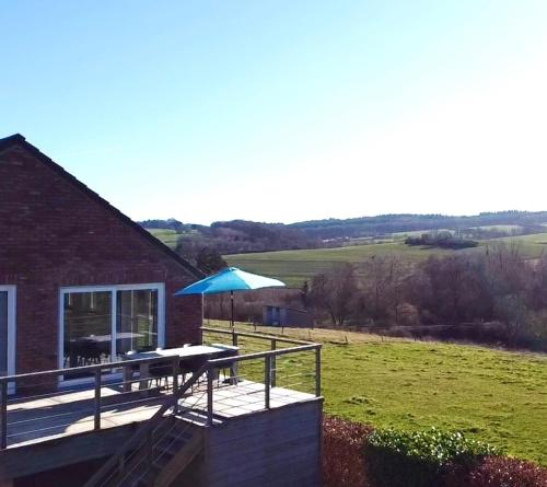 a deck with a blue umbrella and a table at Huis met zonneterras, tuin en panoramisch uitzicht in Wellin