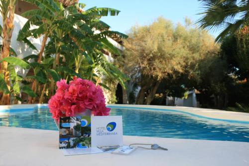 a table with a bouquet of pink flowers and a card at Hotel Villa Mediterranea in Noto Marina