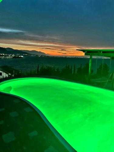 a green swimming pool with a sunset in the background at Magical view, Villa Asproneri, Kamena Vourla in Kamena Vourla