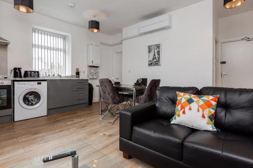 a living room with a black couch and a kitchen at York Villas Free Parking Included in Liverpool