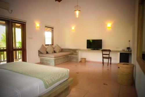 a bedroom with a bed and a couch and a television at Kingfisher Bamboo Garden Villa in Unawatuna