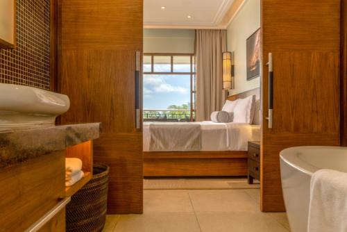 a bathroom with a bedroom with a bed and a tub at Savoy Seychelles Resort & Spa in Beau Vallon