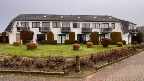 a large white house with a yard with bushes at Ferienwohnung am Kormoranweg in Dorum Neufeld