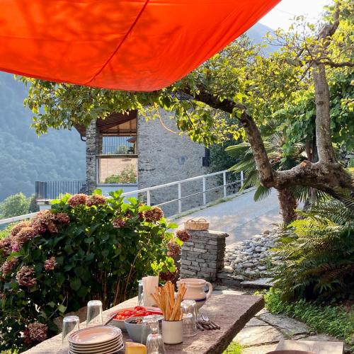 a table with plates of food under an orange umbrella at Casa Bruja Tradizionale Rustico Ticinese in Mergoscia