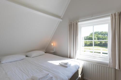 a white bedroom with a bed and a window at Hello Zeeland - Vakantiehuis Brouwerijweg 43-3 in Domburg