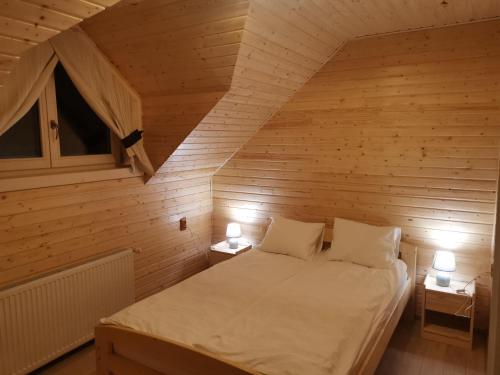 a bed in a wooden room with two lamps at Cabana Katica 2 vendégház in Borzont