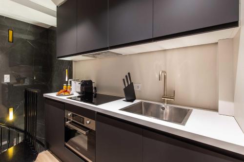 La cuisine est équipée d'un évier en acier inoxydable et de placards noirs. dans l'établissement Cosy Appart - 3BR6P Jardin du Luxembourg Odeon, à Paris