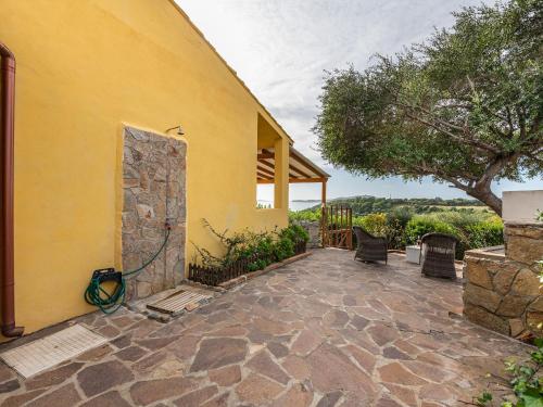 a yellow house with a stone patio with a tree at VILLA CLAUDIO e LUNETTA in Villasimius