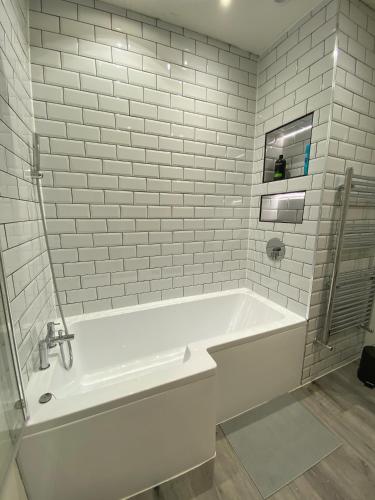 a white bath tub in a bathroom with white tiles at A spacious & modern 3-bed home in Blackburn