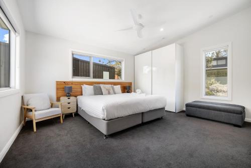 a bedroom with a bed and a chair and windows at Stillwater Chalet B Crackenback in Crackenback