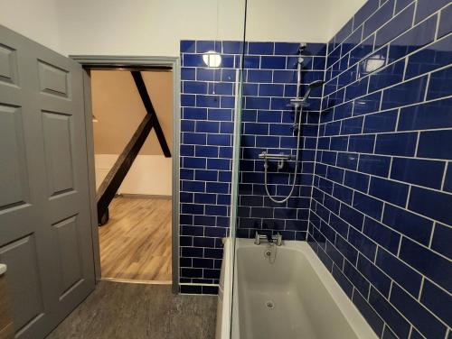 ein blau gefliestes Bad mit einer Badewanne und einer Tür in der Unterkunft The Olde Chapel 2 Bedroom Flat in Market Deeping