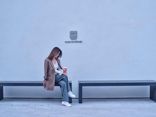 FAV TOKYO Nishinippori في طوكيو: امرأة تجلس على مقعد على الحائط