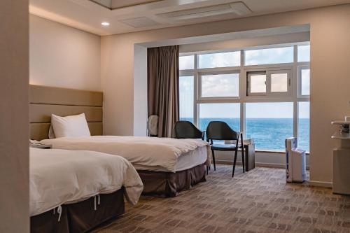 a hotel room with two beds and a large window at Cocoon Hotel in Jeju