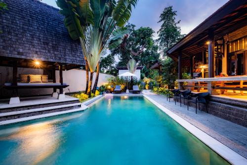 a swimming pool in front of a building with a house at Villa Frangipani Seminyak in Seminyak