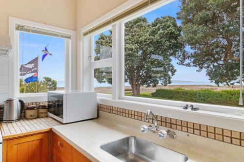 een keuken met een wastafel en 2 ramen met uitzicht op de oceaan bij Whare Nui on Rennie - Thames Holiday Home in Thames