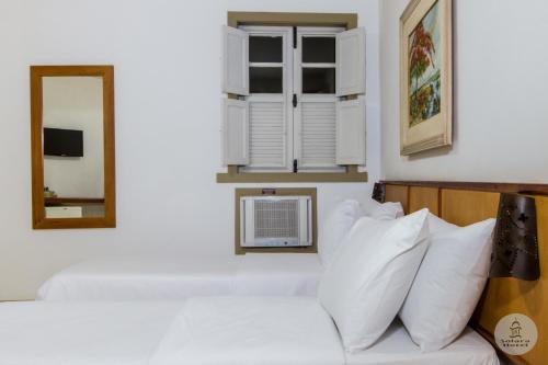 Camera dotata di letto con cuscini bianchi e specchio. di Solara Hotel a São João del Rei