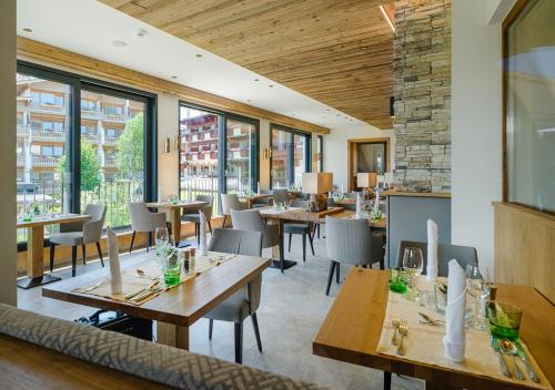 un restaurante con mesas y sillas de madera y ventanas en Hotel Alpina Wellness & Spa Resort en Kössen