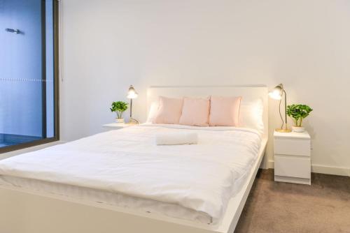 Una cama blanca con almohadas rosas y un ordenador portátil. en Sydney CBD Modern 2 bedroom Apartment, en Sídney