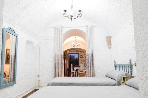 Habitación blanca con 2 camas y espejo. en Casa Cueva Picoesquina, en Guadix
