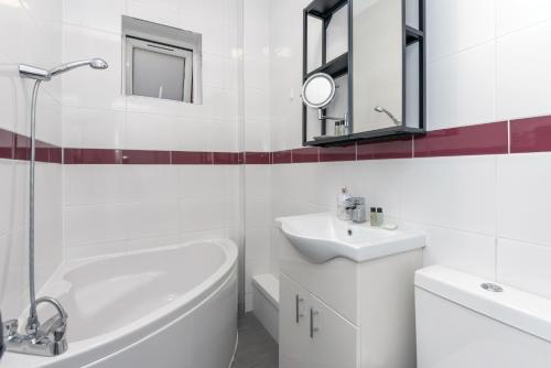 a white bathroom with a sink and a tub and a mirror at Taylor's Apartment Wimbledon in London