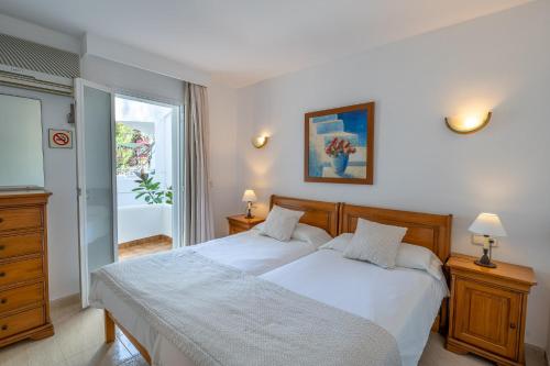 um quarto com uma cama com lençóis brancos e uma janela em Apartamentos Los Tilos em Paguera
