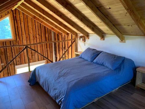 1 dormitorio con 1 cama azul en una habitación de madera en "Refugio Pulli" Tierra y naturaleza, en Villarrica