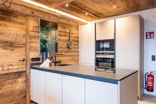 a kitchen with white cabinets and wood walls at Hideaway Dachstein West by ALPS RESORTS in Sankt Martin am Tennengebirge