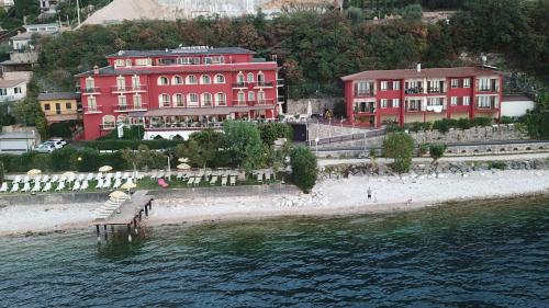 un groupe de bâtiments rouges sur une plage au bord de l'eau dans l'établissement Hotel Merano, à Brenzone