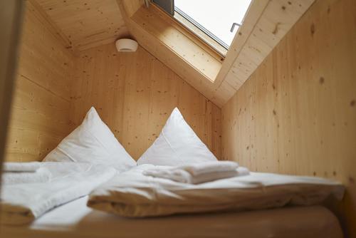 1 cama con almohadas blancas en una habitación con ventana en Wellnester Tiny Houses and Retro-Caravan by the lake in Losheim am See en Losheim