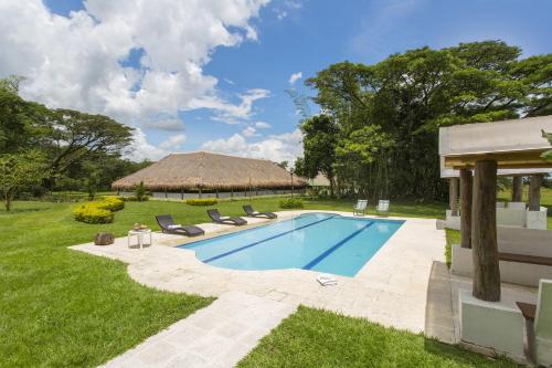 a swimming pool in a yard with chairs and a hut at Hotel Cinaruco Caney in Villavicencio