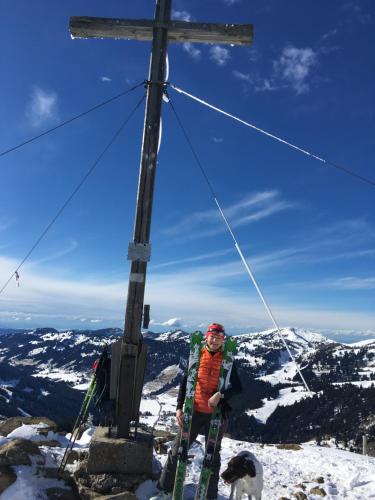 a man standing next to a cross on a mountain at Gemütliche Ferienwohnung Bergwiese, 2-Raum, separates Schlafzimmer, schönen Balkon oder Terrasse, Komfort Ausstattung, ruhige Südlage, kostenfrei WLAN und schöne helle Sauna, Brötchenservice, Parkplatz, Hunde auf Anfrage, E-Tankstelle, Sonnenlage in Balderschwang