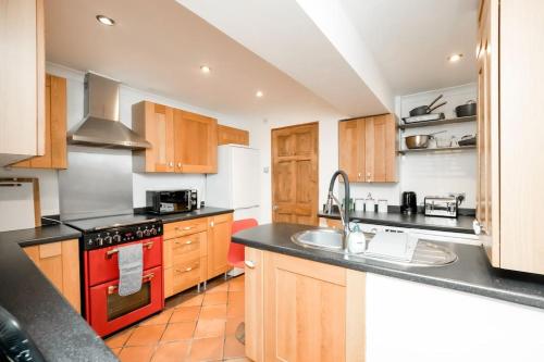 eine Küche mit Holzschränken und einem Backofen mit rotem Kochfeld in der Unterkunft 3 Bedroom home close to town centre with WiFi & garden in Royal Tunbridge Wells