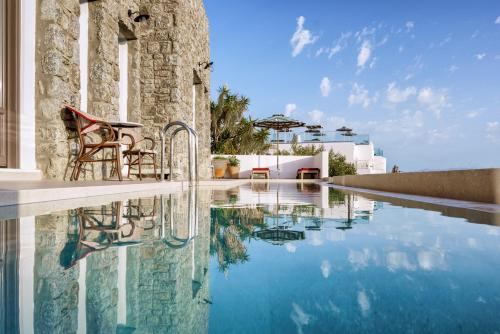 a swimming pool with two chairs next to a building at Pelican Bay Hotel in Platis Gialos