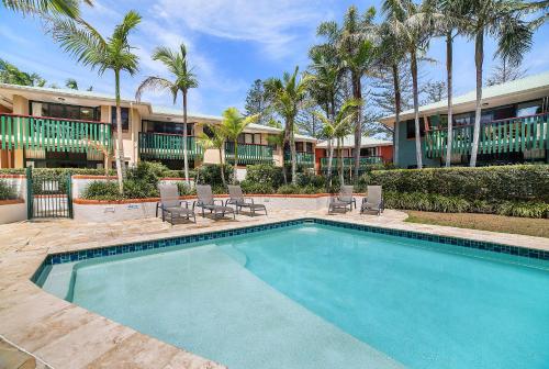 a swimming pool in front of a building with palm trees at The Crest Byron Bay in Byron Bay