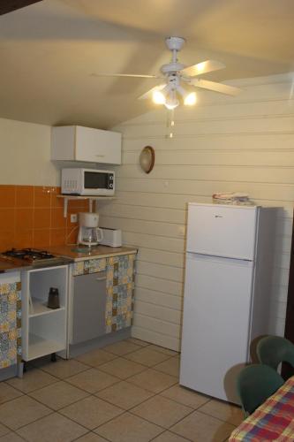 a kitchen with a white refrigerator and a ceiling fan at Gite bagatelle classé 2 étoiles in Sainte-Rose