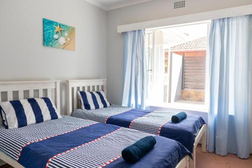 a bedroom with two beds with blue pillows and a window at The Jbaynian Guesthouse in Jeffreys Bay
