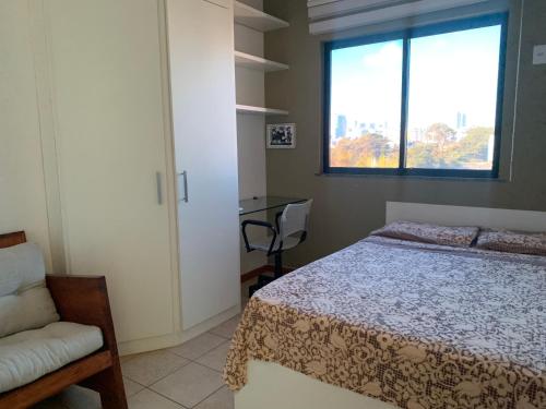 um quarto com uma cama, uma cadeira e uma janela em Apartamento no Rio Vermelho - Bairro Boêmio de Salvador em Salvador