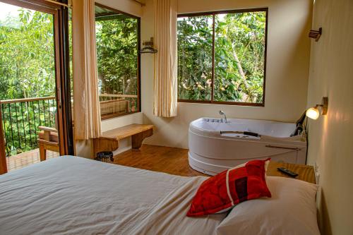 Schlafzimmer mit einem Bett, einer Badewanne und einem Fenster in der Unterkunft Cabañas Armonía y Jardín de Orquídeas in Mindo