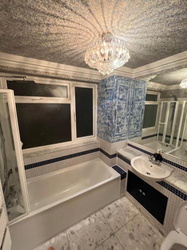 un bagno con vasca, lavandino e lampadario a braccio di TJ Homes - One double bed room with garden view - Next to tube station a Ruislip