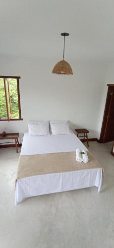 a bedroom with a large white bed with a white cat laying on it at Pousada Aroeira in Itaúnas