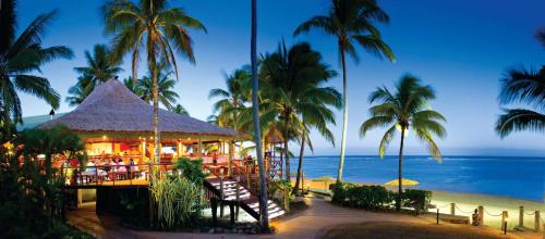 a restaurant on the beach with palm trees and the ocean at Outrigger Fiji Beach Resort in Korotogo