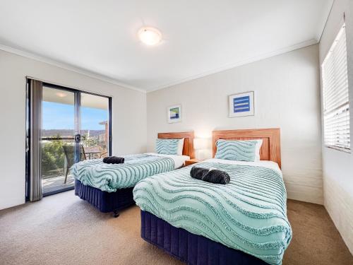 two beds in a room with a window at Seachange Apartments Merimbula in Merimbula