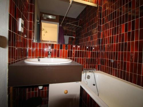 La salle de bains est pourvue de carrelage rouge, d'un lavabo et d'une baignoire. dans l'établissement Studio cabine 4 couchages à 150m des pistes avec terrasse et parking - Auris en Oisans - FR-1-297-3, à Auris